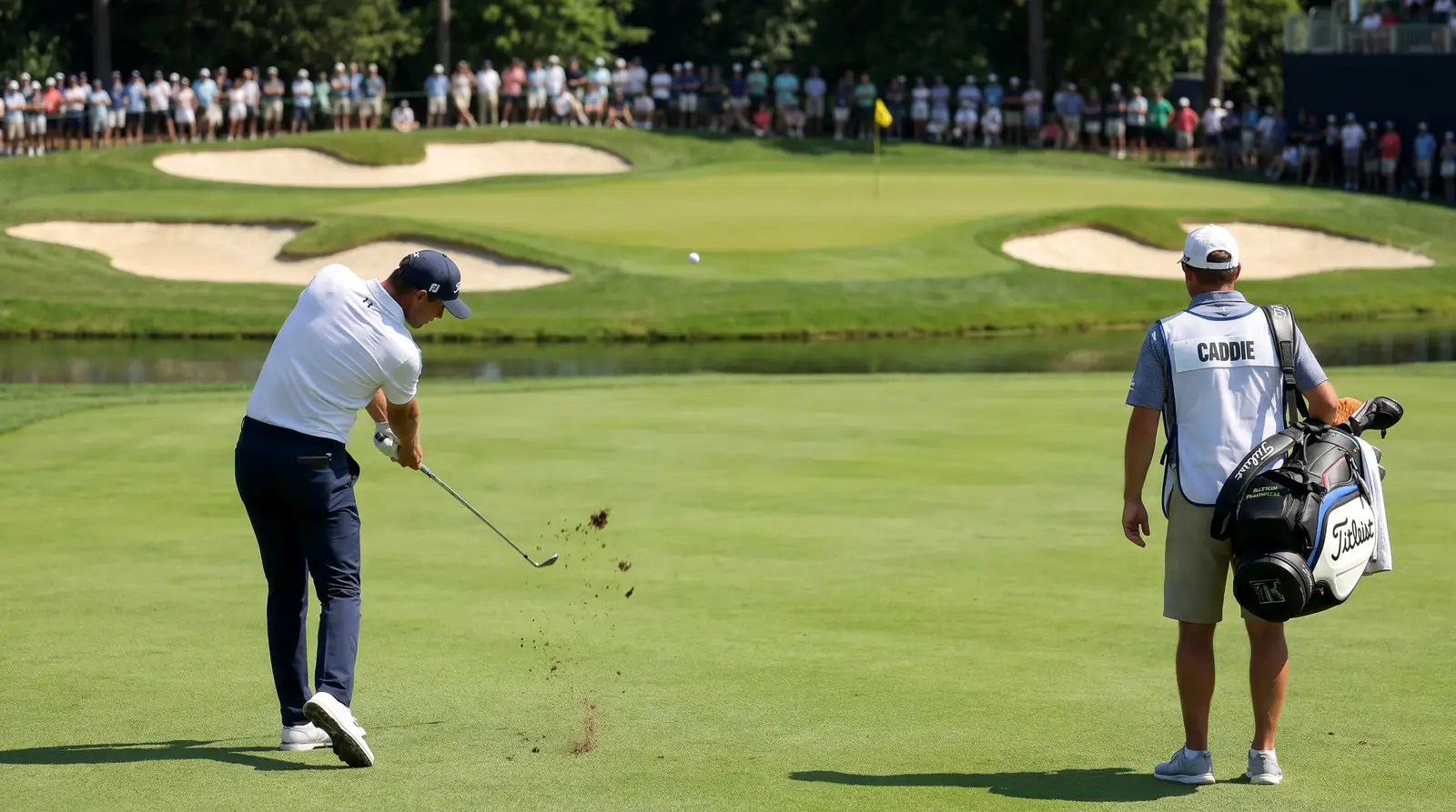Professional golfer striking an iron approach shot from the fairway towards a guarded green