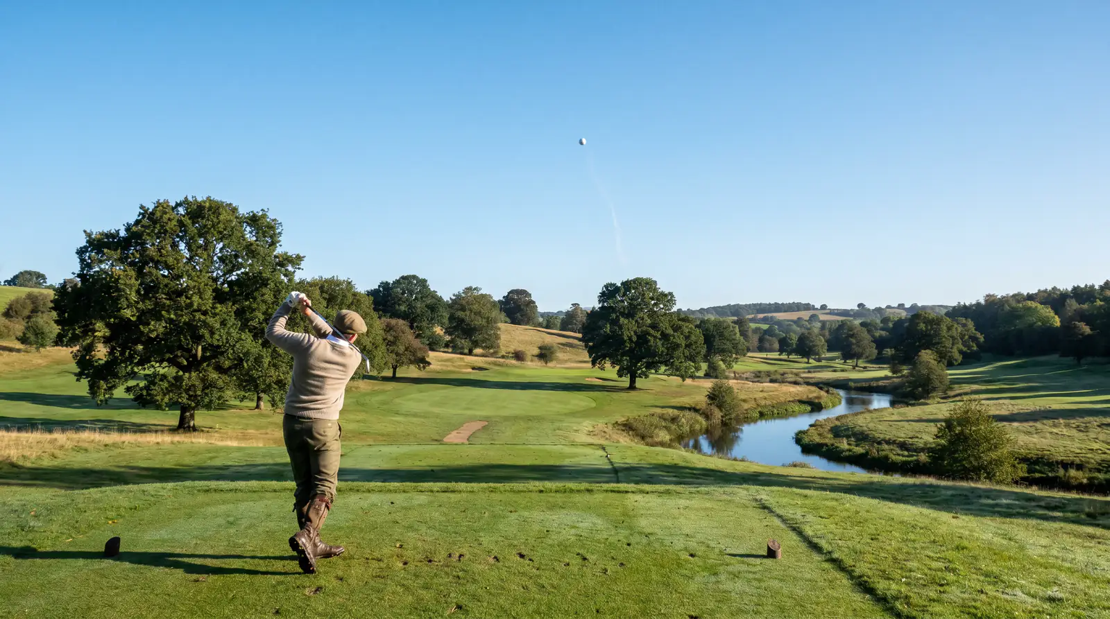 Long drive ball flight mid-air against a clear sky at a UK tournament tee