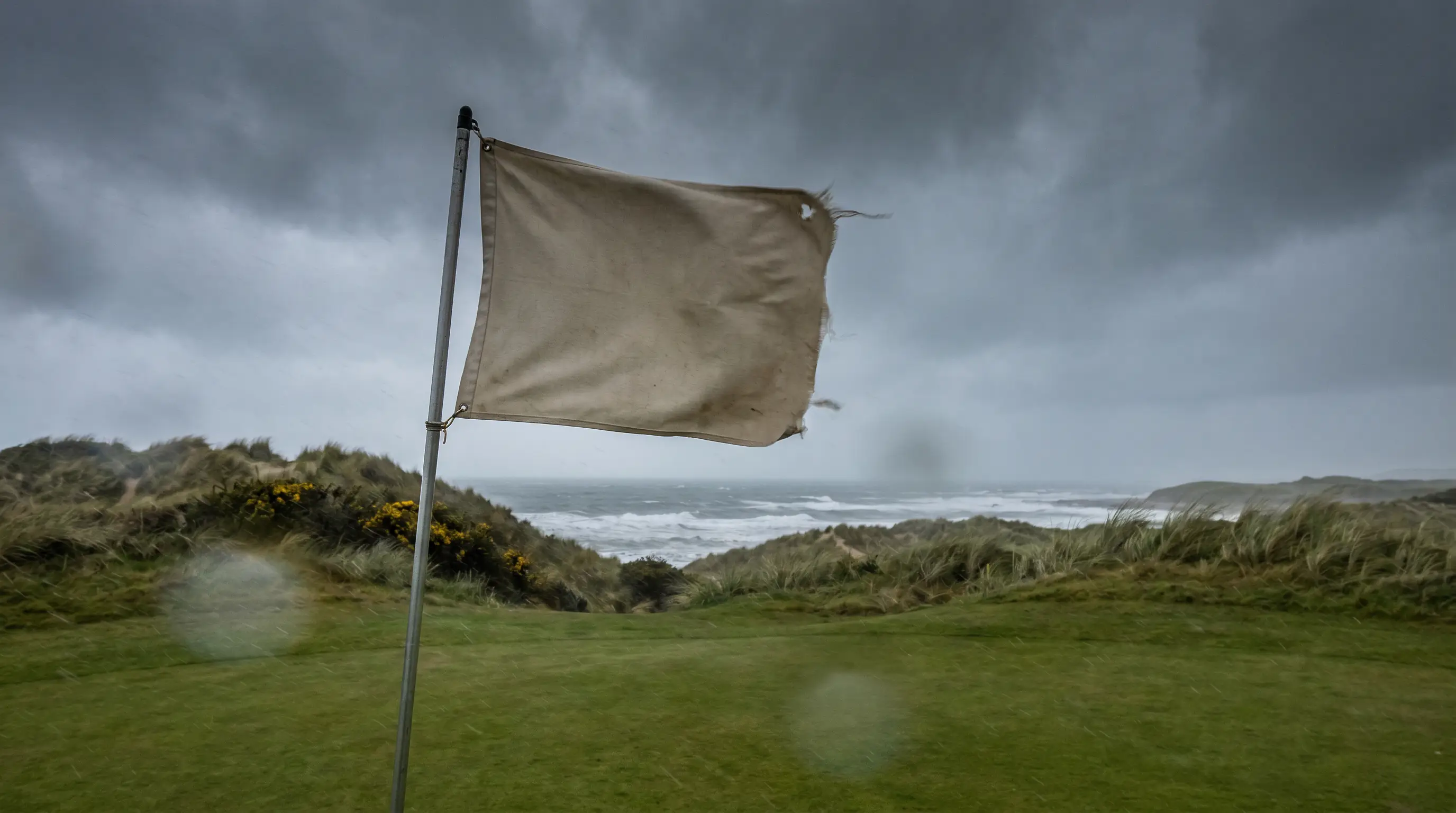 Flag whipping in heavy wind on a links green at a UK tournament